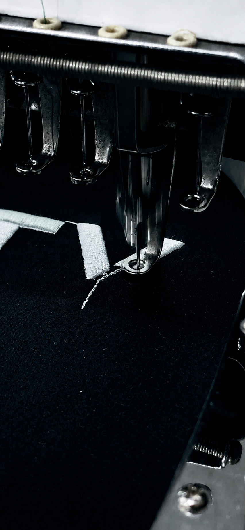 Close-up of an Al Zarkan Factory embroidery machine needle stitching a white logo onto black uniform fabric